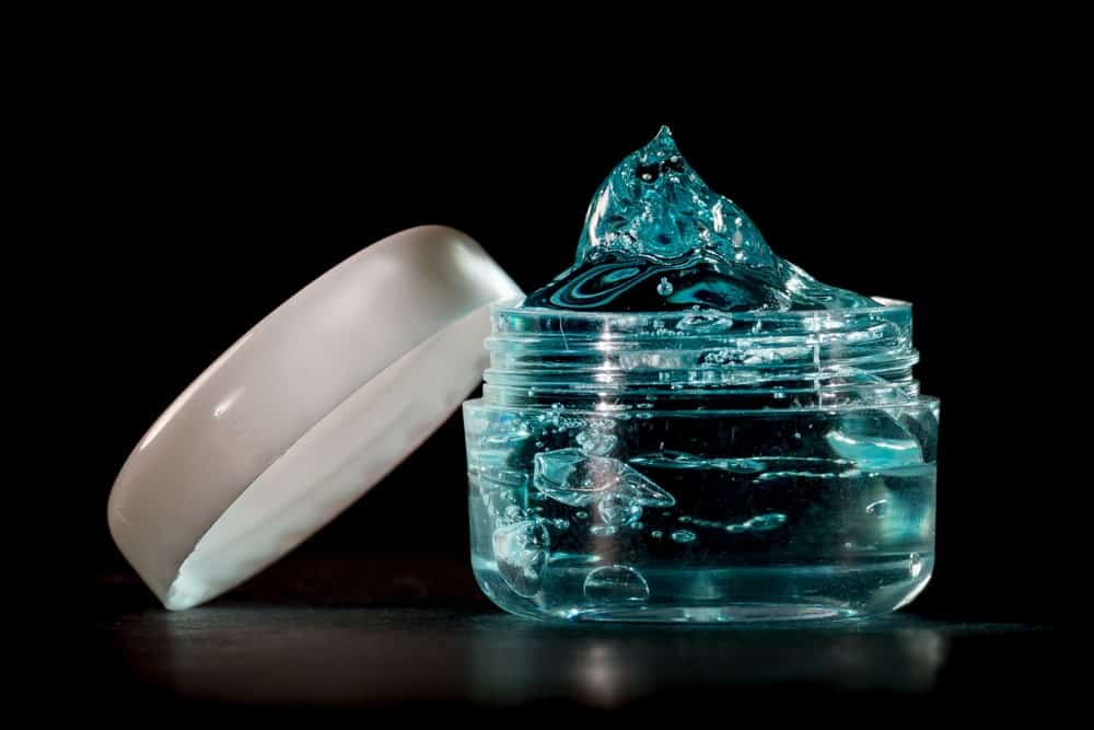 An opened transparent tub of gel against the black background.