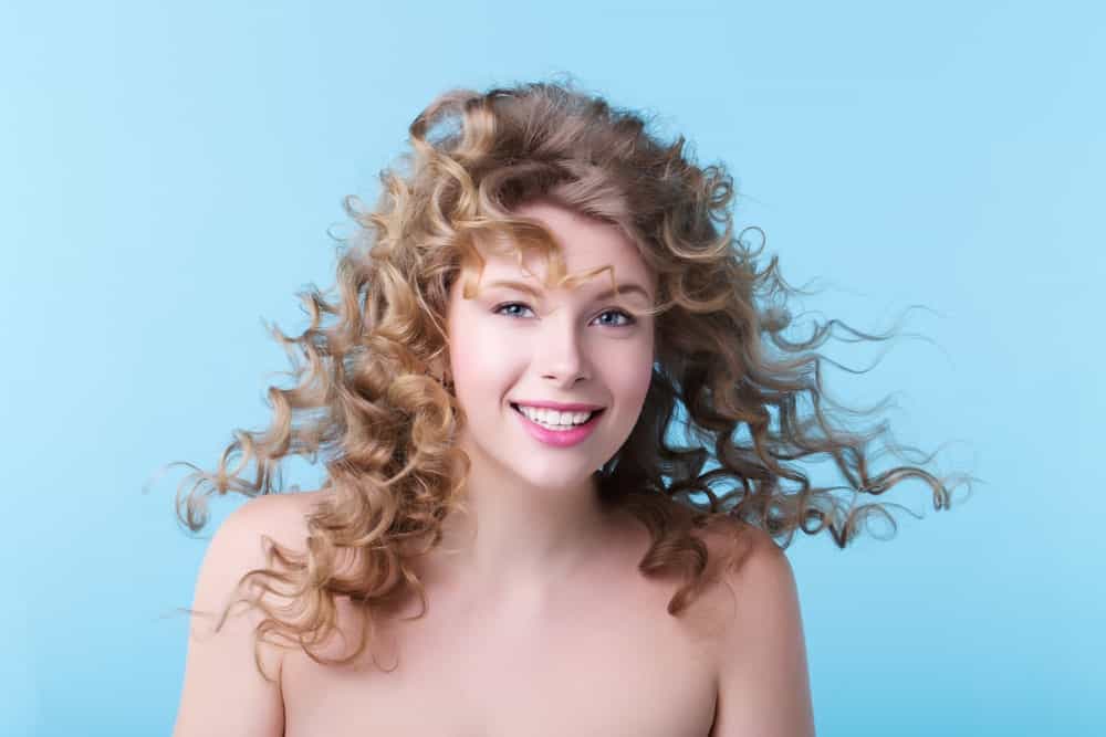 Woman with long curly hairstyle against a pale blue background.