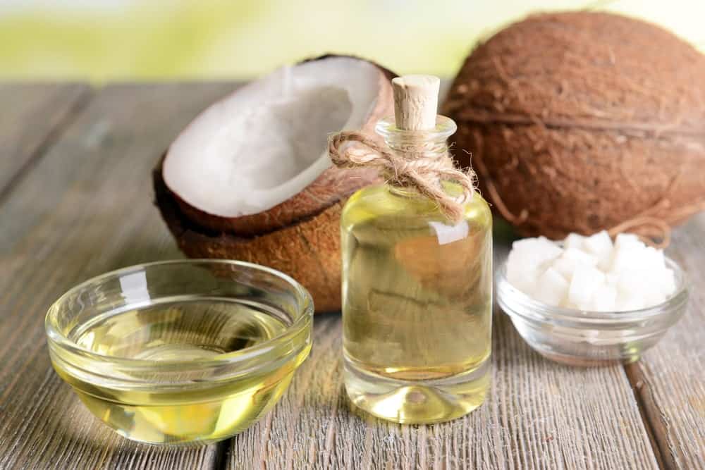 Coconut oils next to fresh coconuts on a wooden table.