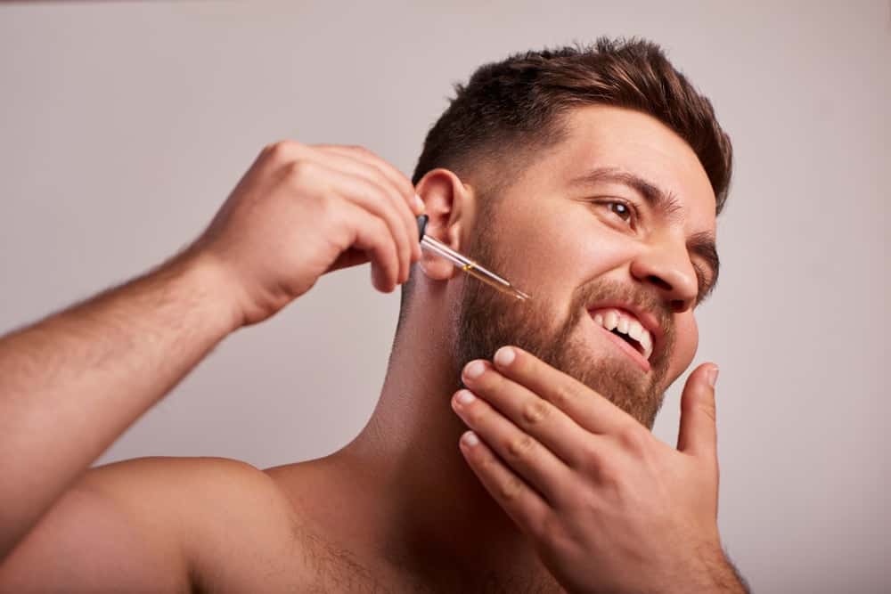 A bearded man applying coconut oil to his beard.