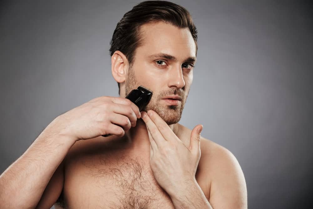 A man shaving his beard using an electric razor.