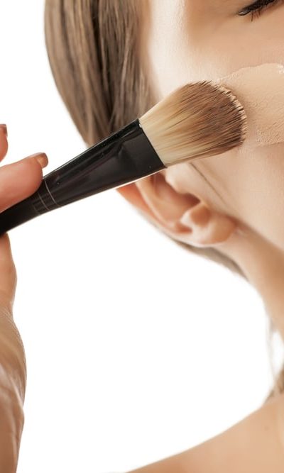 A woman applying brush makeup on her face.