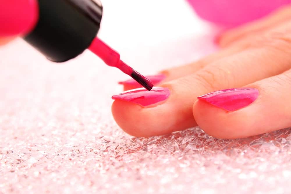 A close look at a woman putting on pink nail polish.