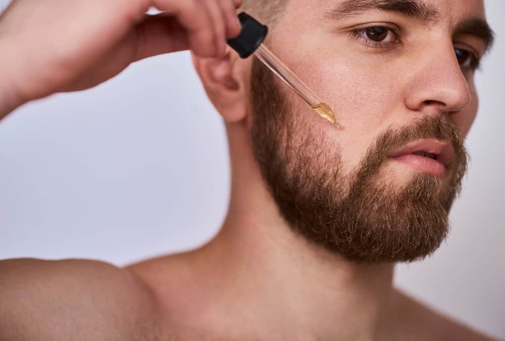 A bearded man putting beard oil on his beard.