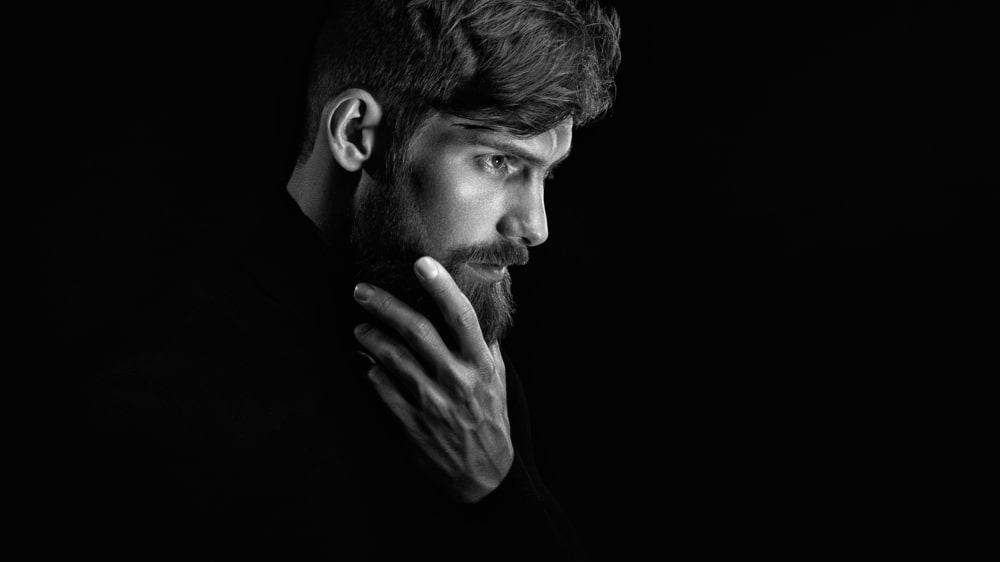 A man stroking his beard against a black background.