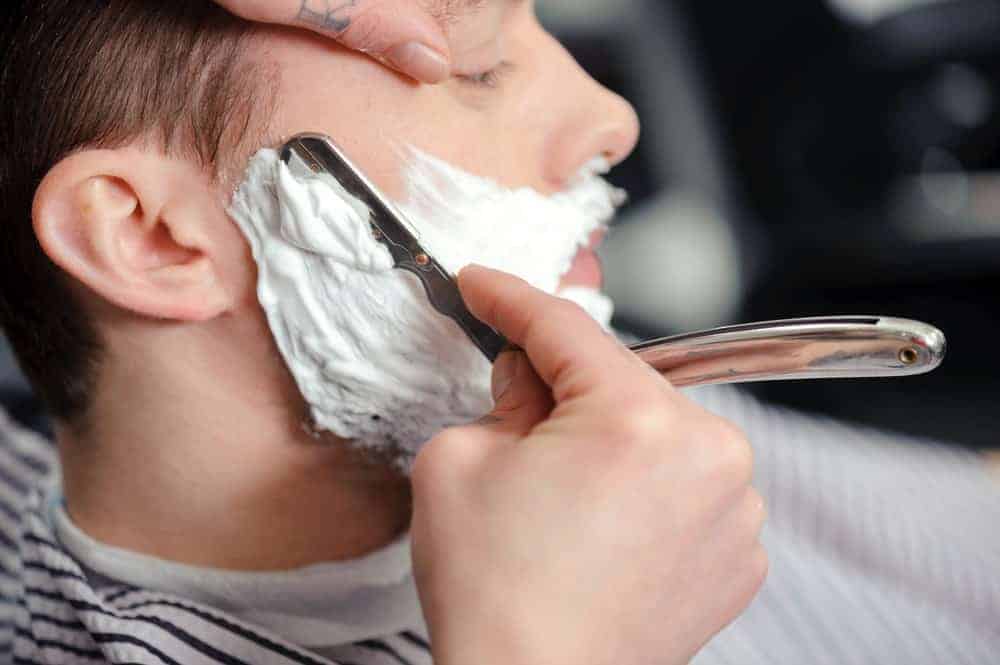Barber shaving the beard of his customer using a straight razor.