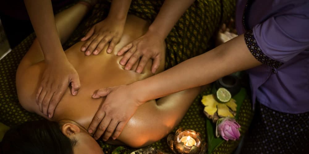 A couple of massage therapists applying Burmese massage to a woman.