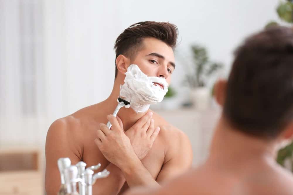 A close look at a man shaving in front of the bathroom mirror.