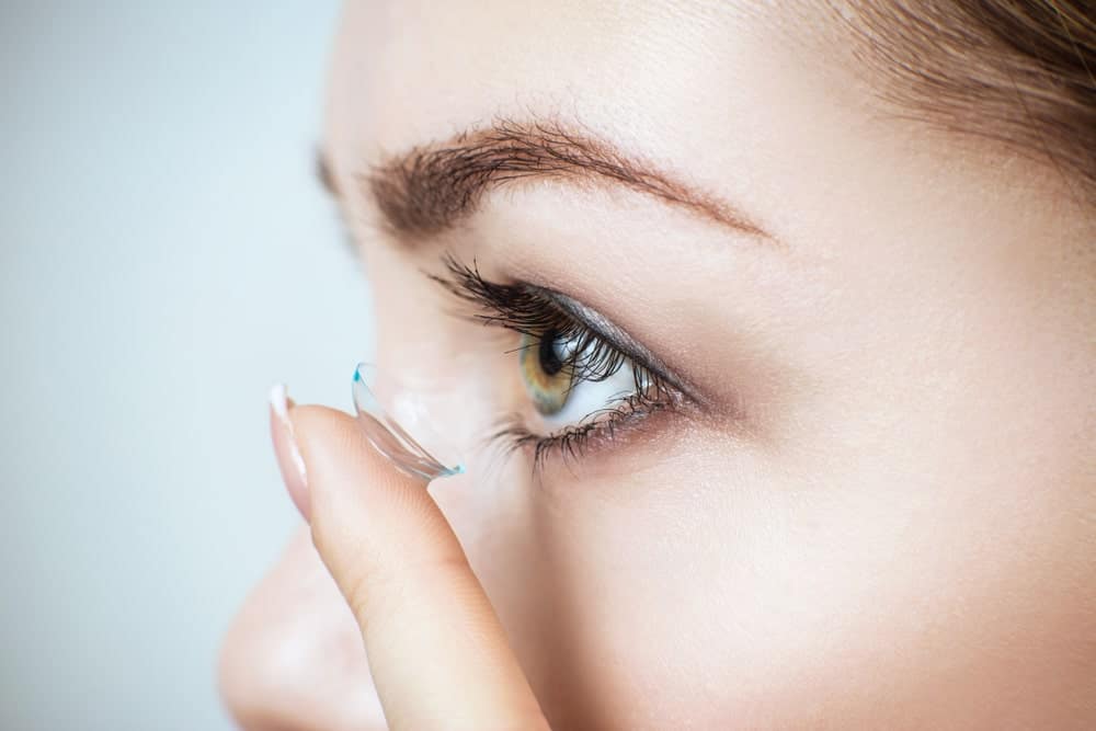 Woman putting clear contact lens in her left eye.