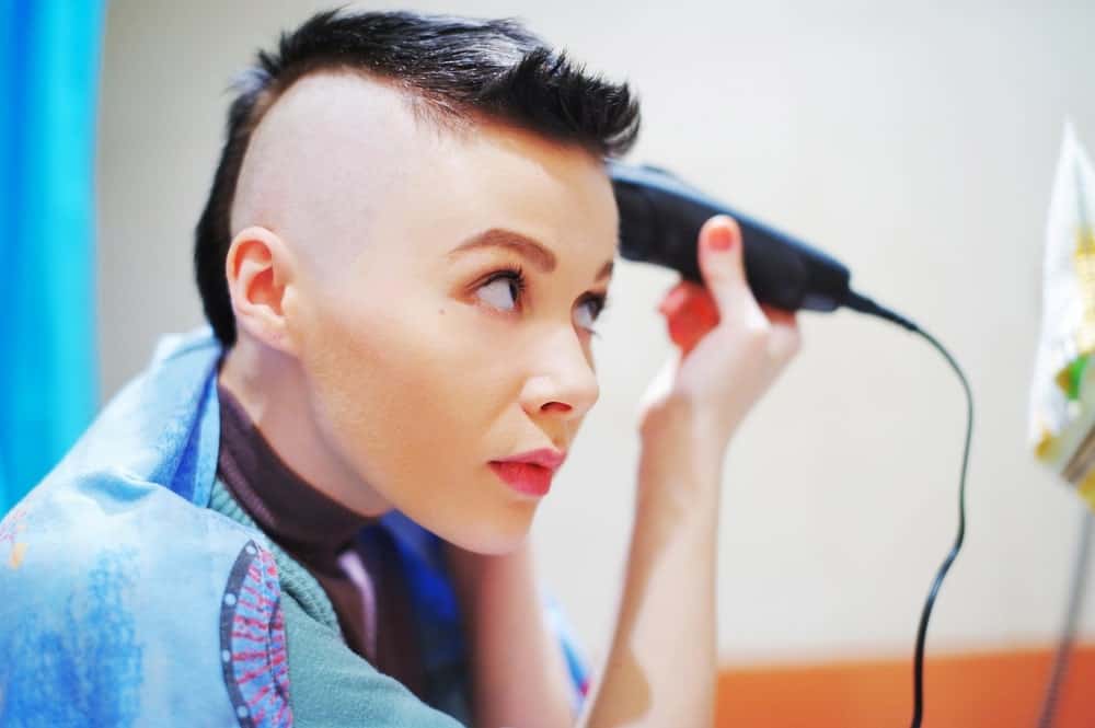 A woman shaving her head in front of the mirror.