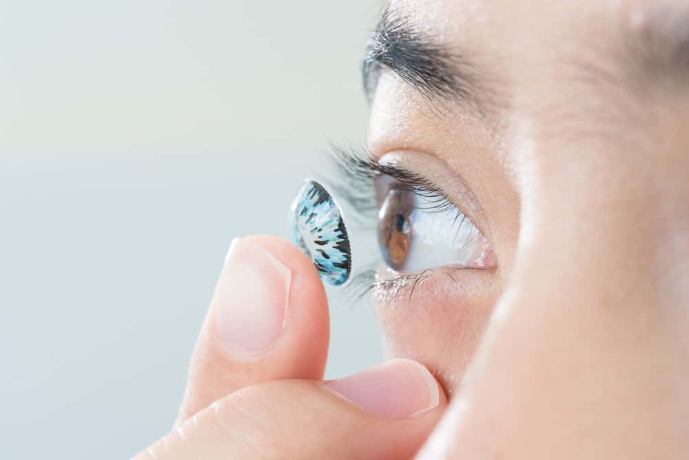 Woman putting colored contact lens in her right eye.