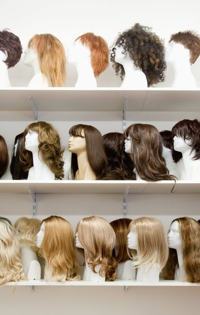 Rows of various wigs on shelves on display at a store.