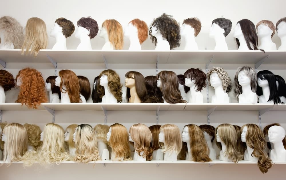 Rows of various wigs on shelves on display at a store.