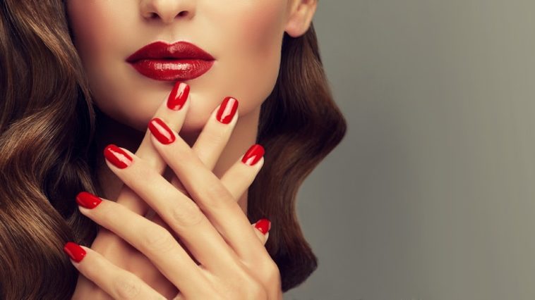 A woman showing off her red fingernails that matches her red lips.
