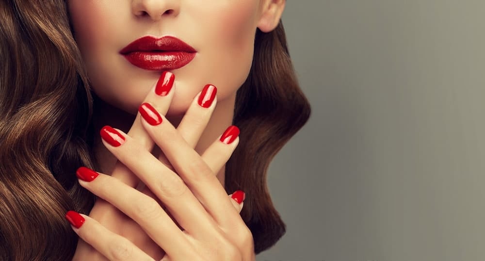 A woman showing off her red fingernails that matches her red lips.