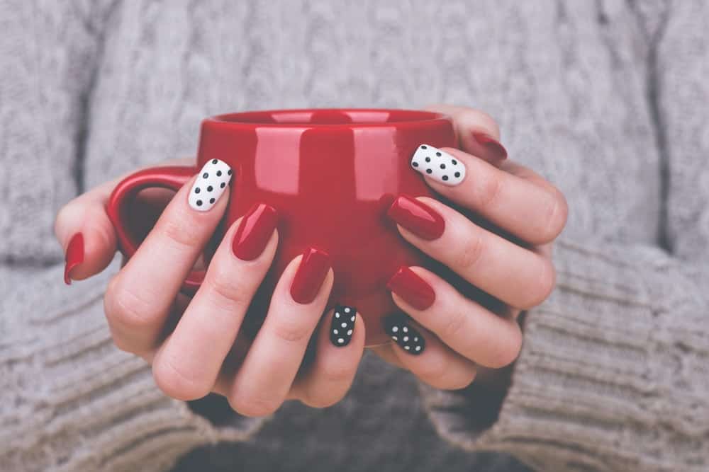 A close look at a woman's hands with various nail polish that is holding a red mug.