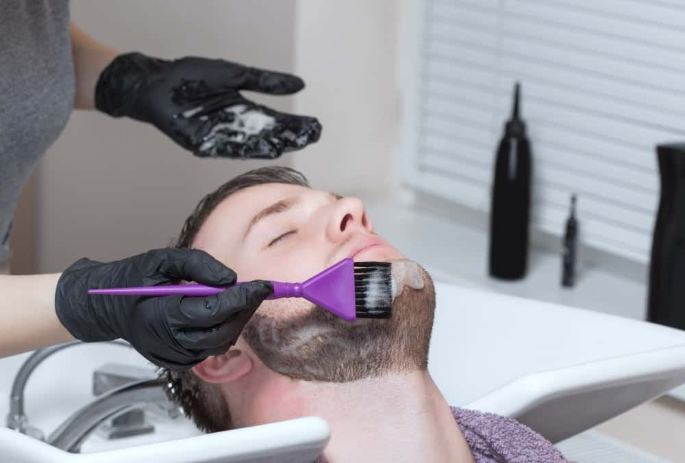 A barber colors the beard of a man.